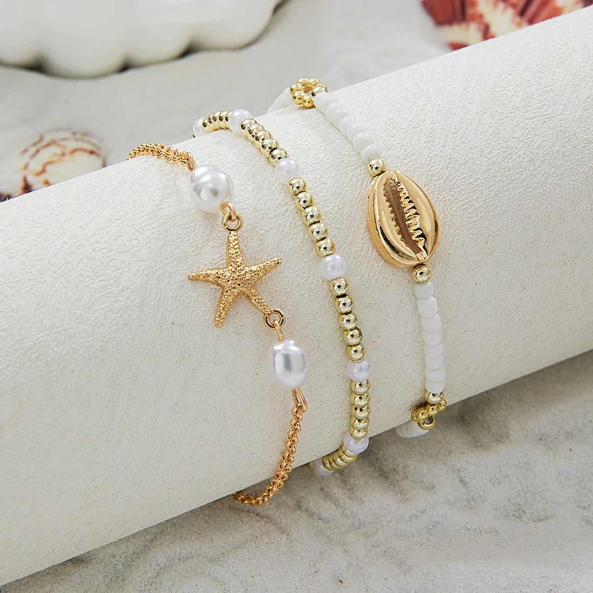 Un ensemble de bracelets de perles or et blanc, présentés sur un rouleau de tissu beige.