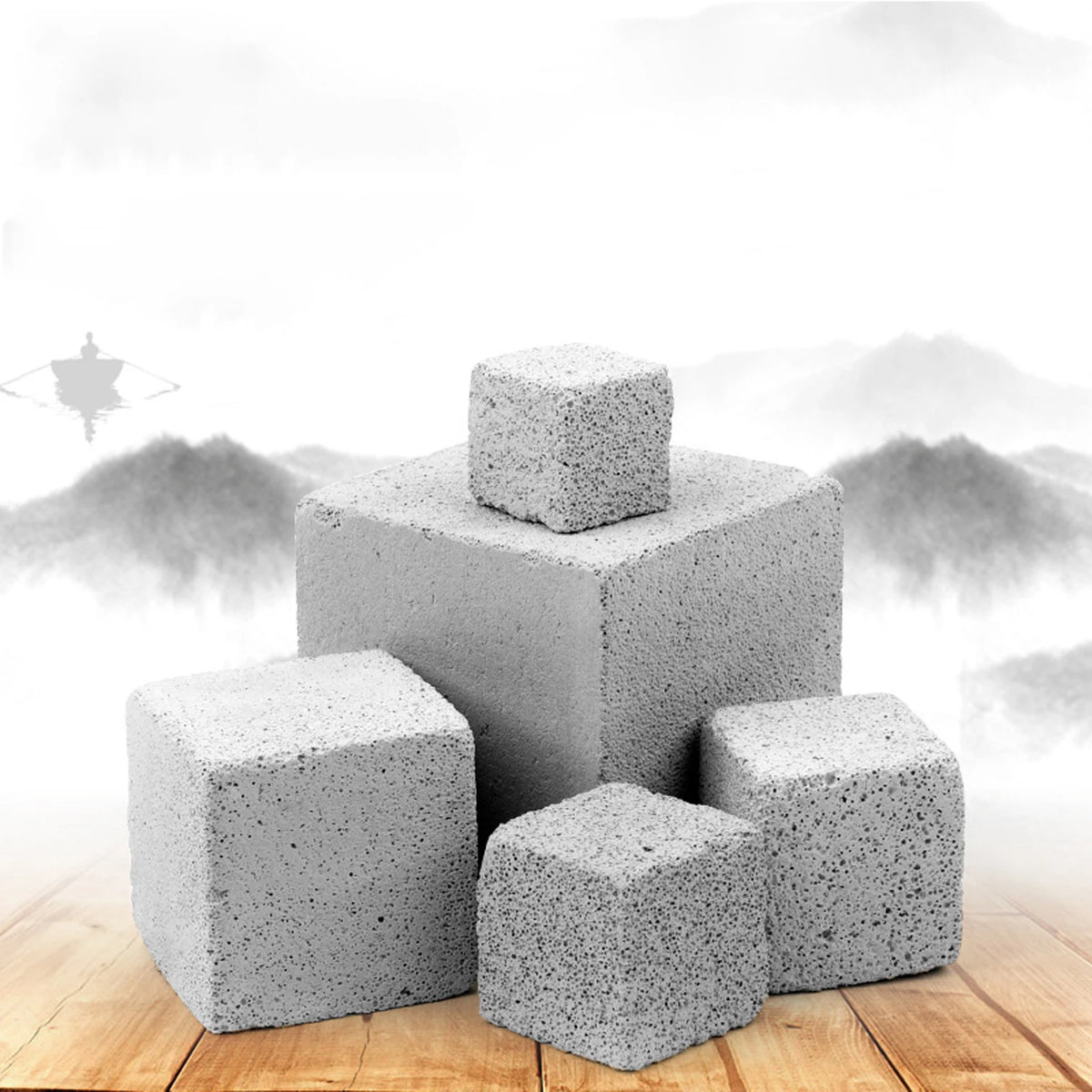 Three gray natural mineral molar stones stacked on a wooden surface against a misty mountain background.