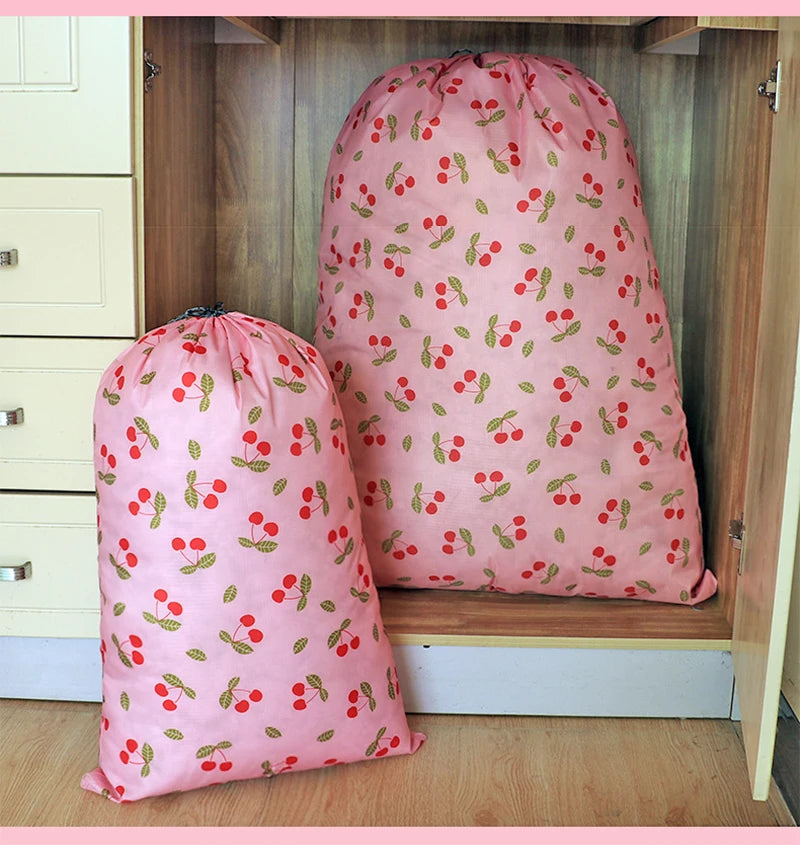 A pink drawstring laundry bag with a red and green cherry pattern is displayed in a wooden cabinet.
