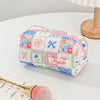 A pink and blue patchwork quilted makeup bag with floral embroidery rests on a white surface next to a makeup brush.