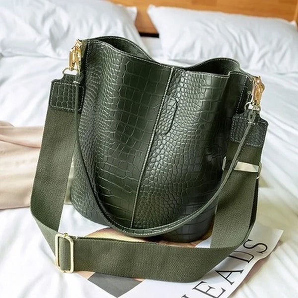 Bolso cruz de estampado de caimán vintage verde oliva oscuro sobre ropa de cama blanca.