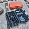 A black waterproof storage box containing various tools and a small orange plastic case on a stone surface.