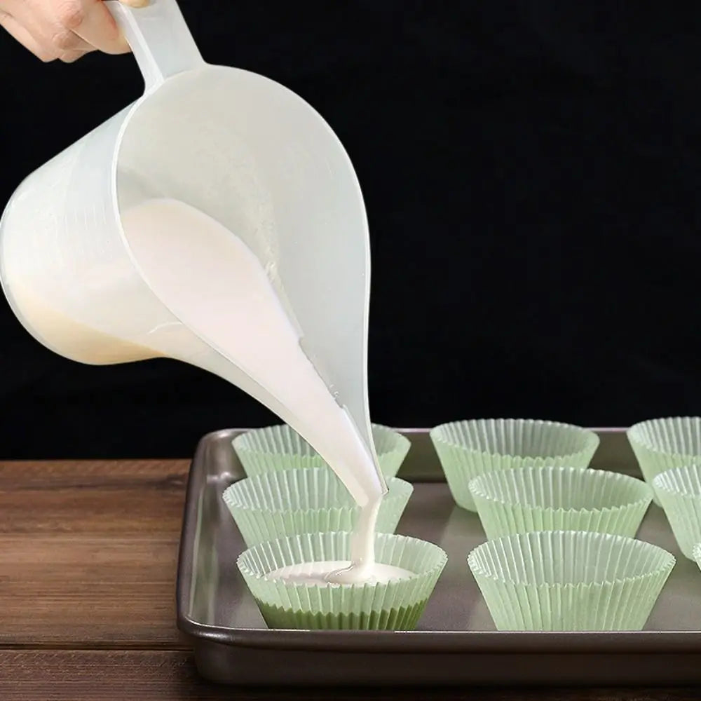 A hand pours white liquid from a plastic measuring cup with a long spout into small green paper cups.
