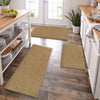 A rectangular natural fiber kitchen runner rug in beige sits on a dark wood floor next to white cabinetry.