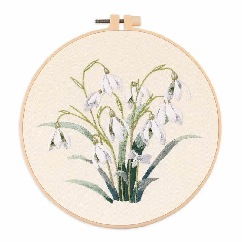 A circular embroidery hoop displaying a delicate floral design of white and pale green spring blossoms.