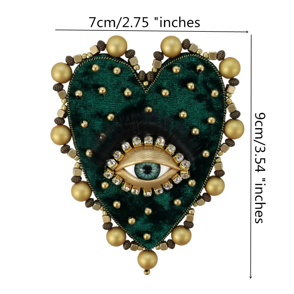 A dark green heart-shaped patch embroidered with black fur and a sparkling gold eye design.