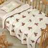 A white cotton gauze baby swaddle blanket with brown bear print, draped over a wooden crib.
