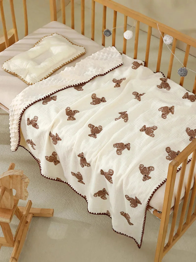 A white cotton gauze baby swaddle blanket with brown bear print, draped over a wooden crib.
