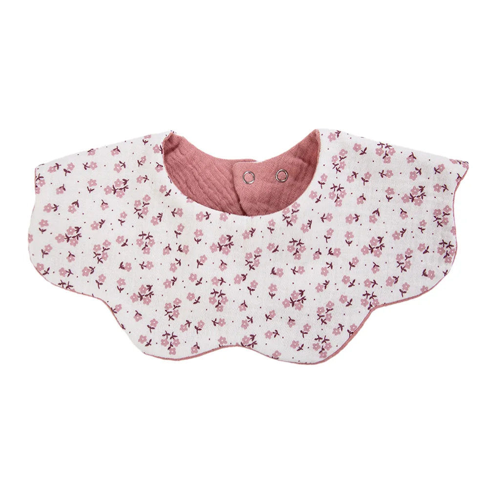 A pink floral patterned muslin cotton baby bib with an adjustable snap closure.