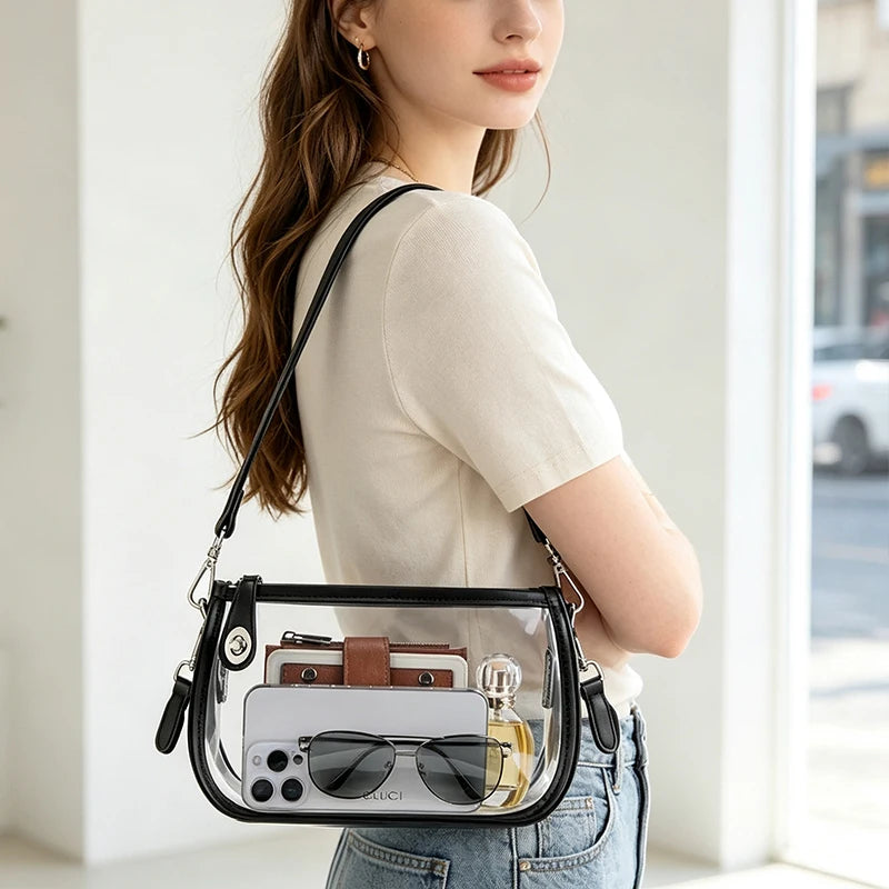 A woman holds a clear PVC shoulder bag with an adjustable strap and a brown leather accent against a bright background.