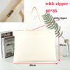 A white canvas tote bag with a handle and zipper, shown next to a fern leaf for scale.