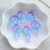 A collection of iridescent blue and pink resin charms shaped like sleeping whales in a white dish.