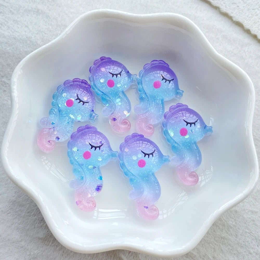A collection of iridescent blue and pink resin charms shaped like sleeping whales in a white dish.