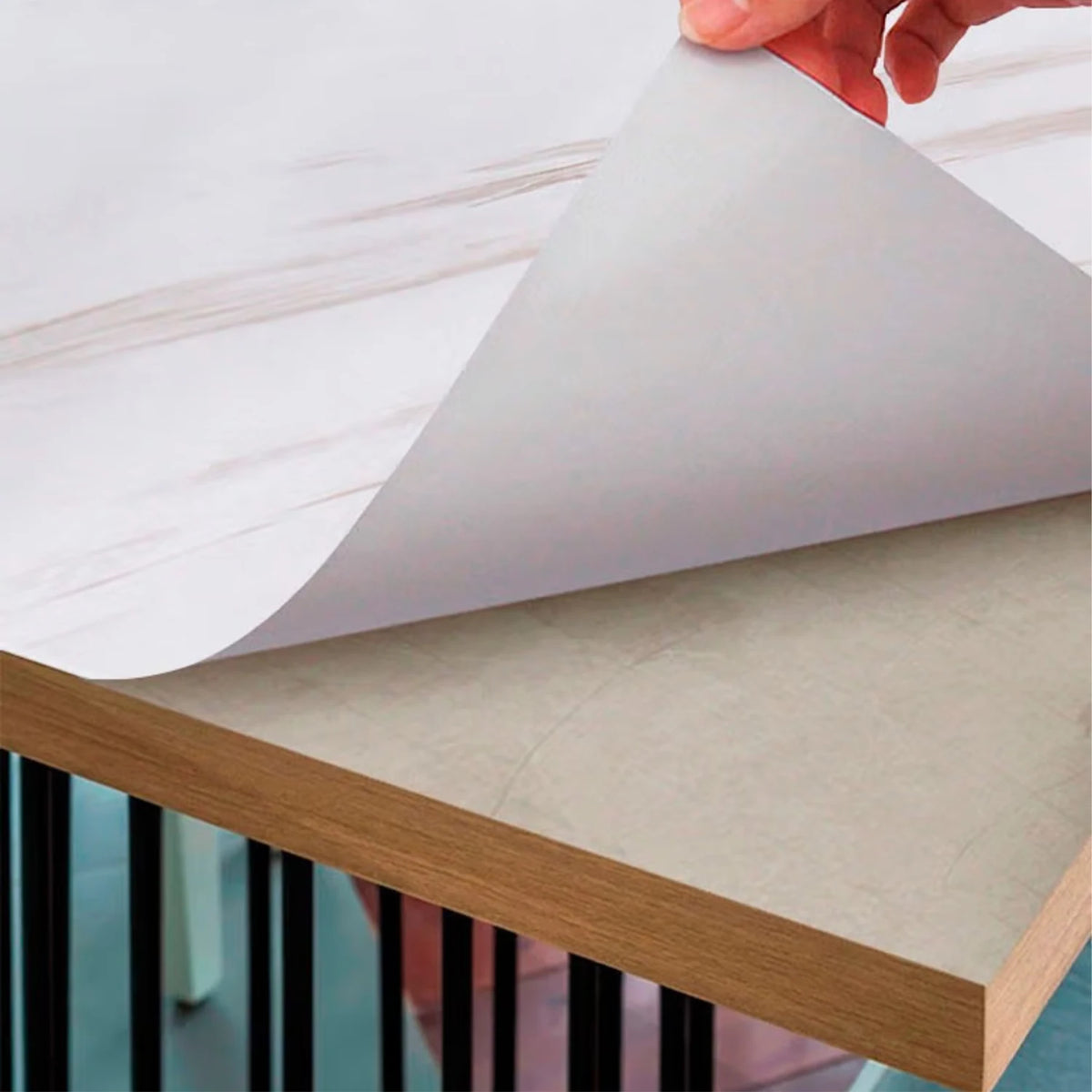 A hand is peeling a sheet of marble peel-and-stick wallpaper onto a wooden surface.