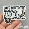 Black embroidered patch with text Love you to the moon and to Saturn on a light gray fabric background