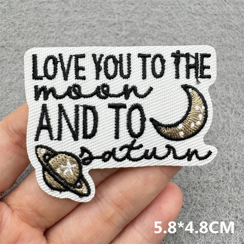 Black embroidered patch with text Love you to the moon and to Saturn on a light gray fabric background