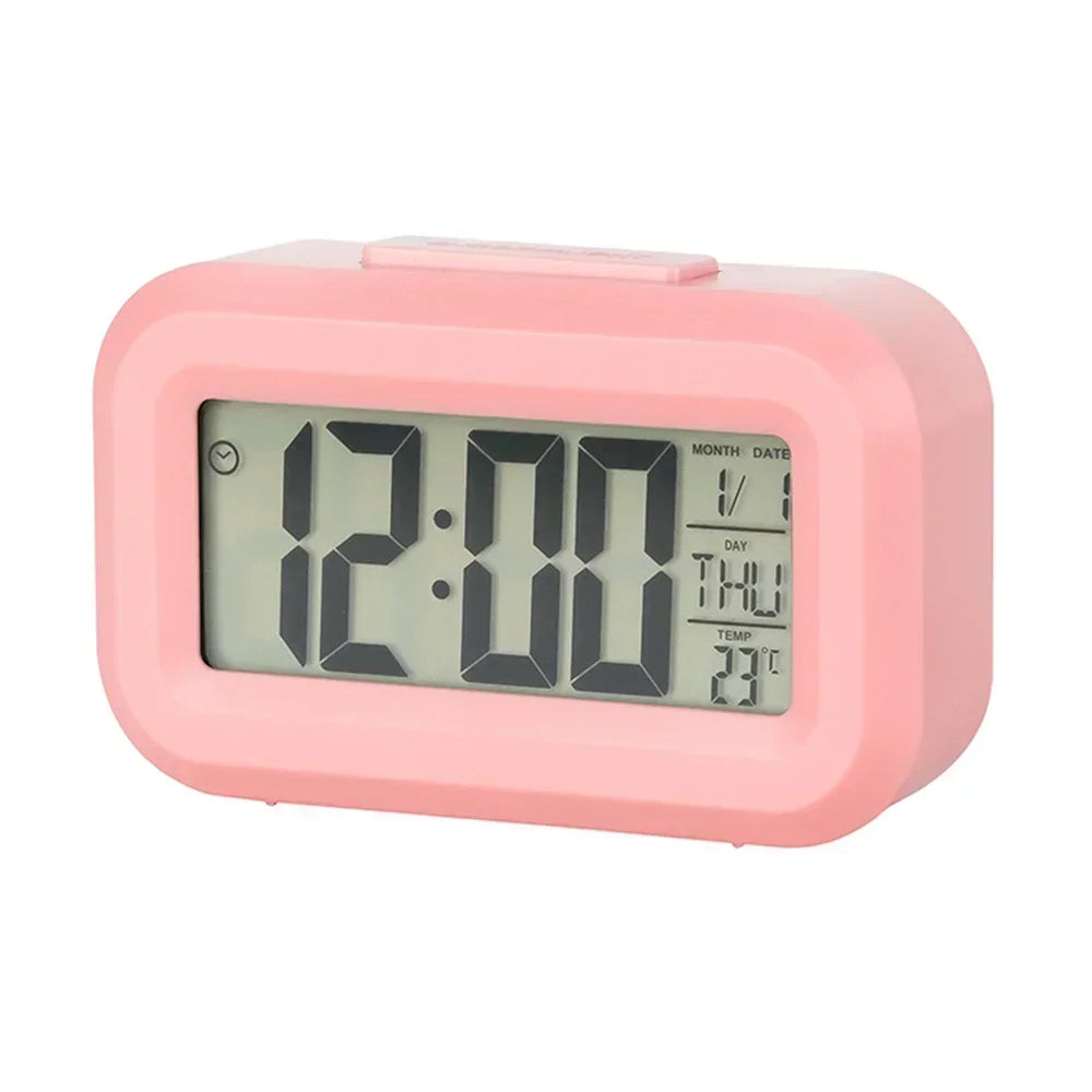 A pink compact LED digital alarm clock displaying 12:00, with a display showing month, date, day, and temperature.