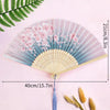 A delicate vintage lace folding hand fan with a pale pink and blue floral design shown against a light pink background.