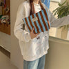 A person holds a striped canvas cosmetic bag with brown and blue stripes against a window background.