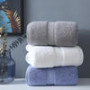 A stack of three bath towels in gray, white, and light blue folded neatly on a white surface.