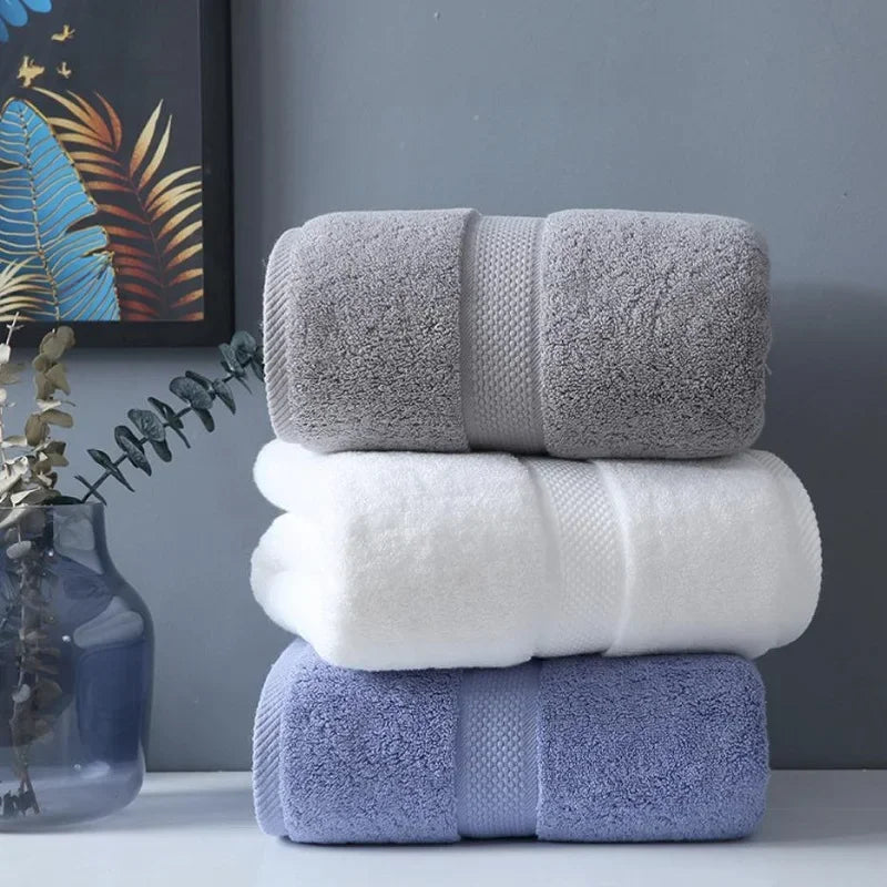 A stack of three bath towels in gray, white, and light blue folded neatly on a white surface.