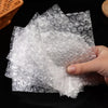 A hand holds a stack of clear bubble mailers filled with white cushioning material.