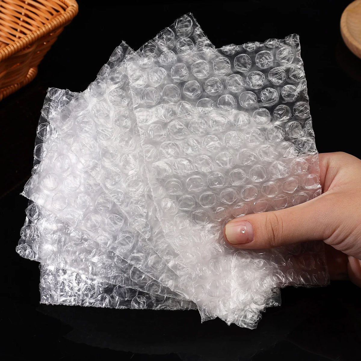 A hand holds a stack of clear bubble mailers filled with white cushioning material.