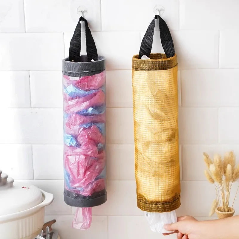 A wall-mounted mesh bag dispenser with colorful plastic bags is displayed against a white tiled wall.