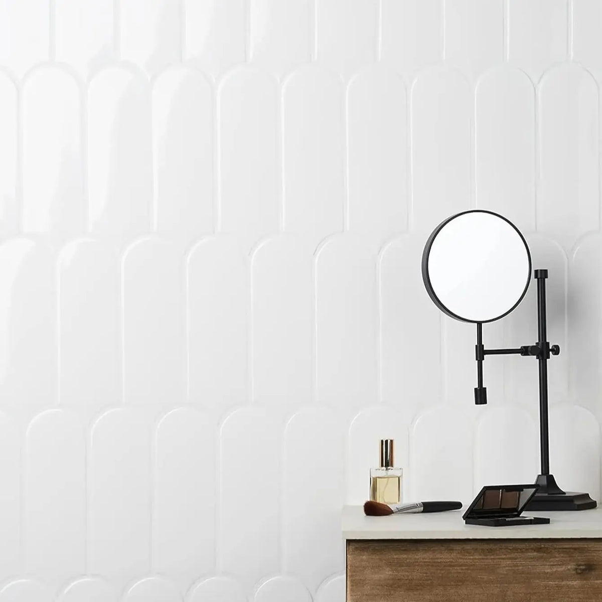 A black magnifying mirror is displayed on a wooden surface against a white, ribbed wall.