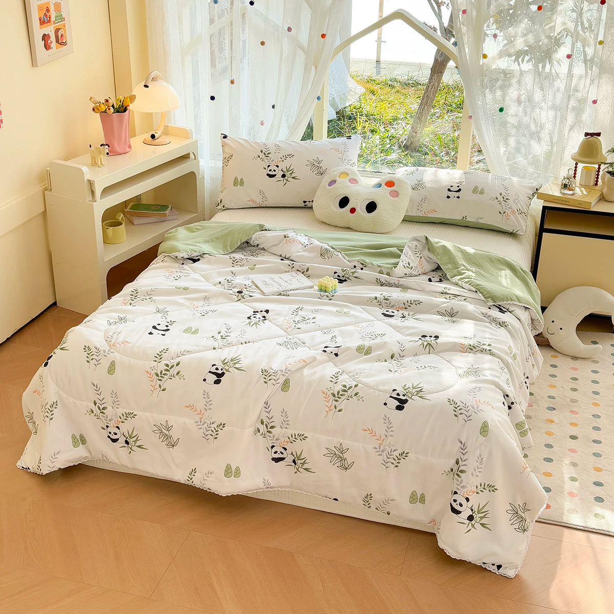A white comforter with a panda print pattern and lace trim is displayed on a bed in a bright room.