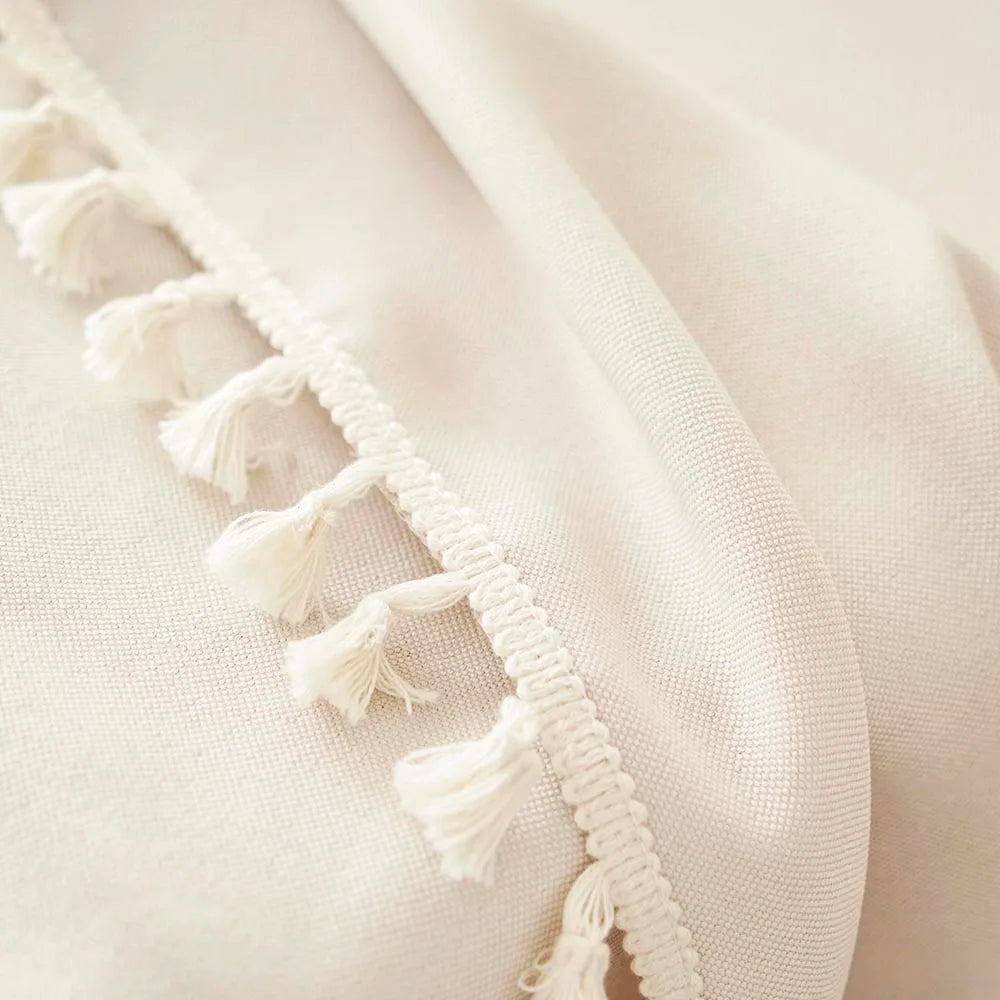 A close-up of a cream-colored farmhouse tablecloth with white cotton tassels along the edge.