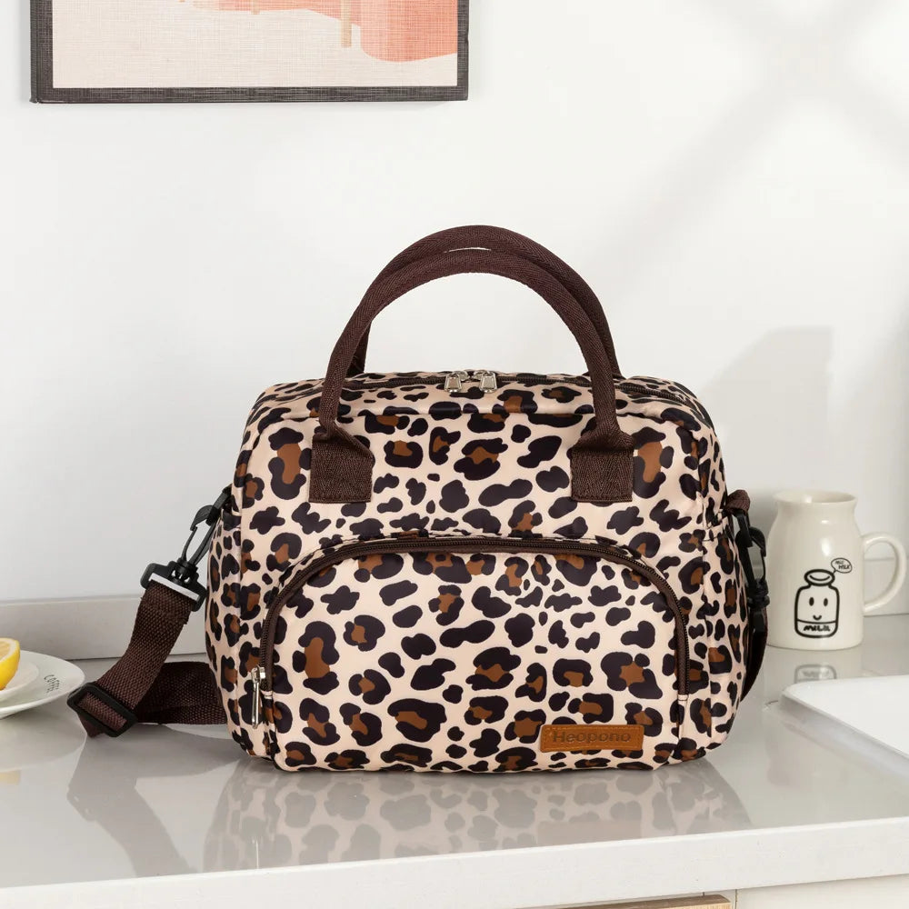 A brown and black leopard print insulated picnic lunch bag with a cross-body strap resting on a white surface.
