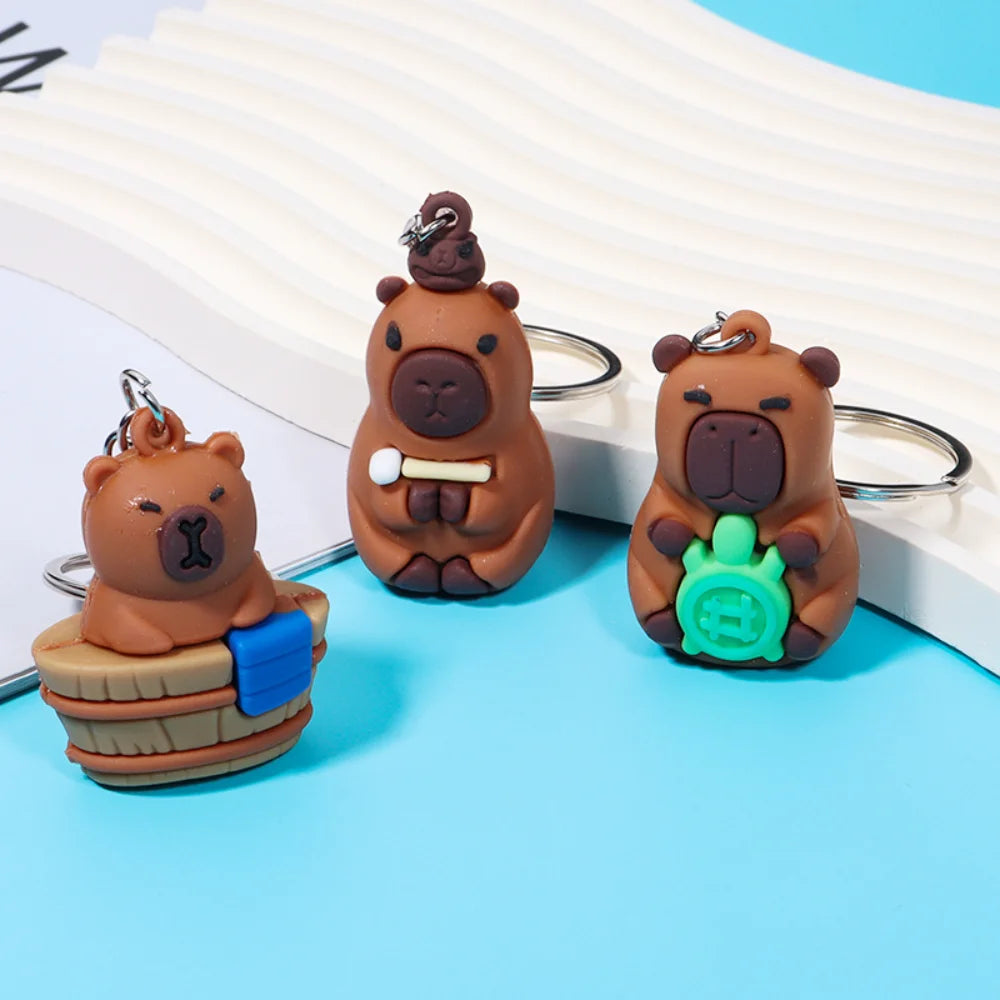 Three adorable brown bear keychain charms with different accessories displayed on a light blue background.