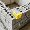 A yellow masonry line corner clip is attached to a gray concrete block forming a wall structure.