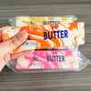 A hand holds a butter fidget stick squishy toy packaged in clear plastic.
