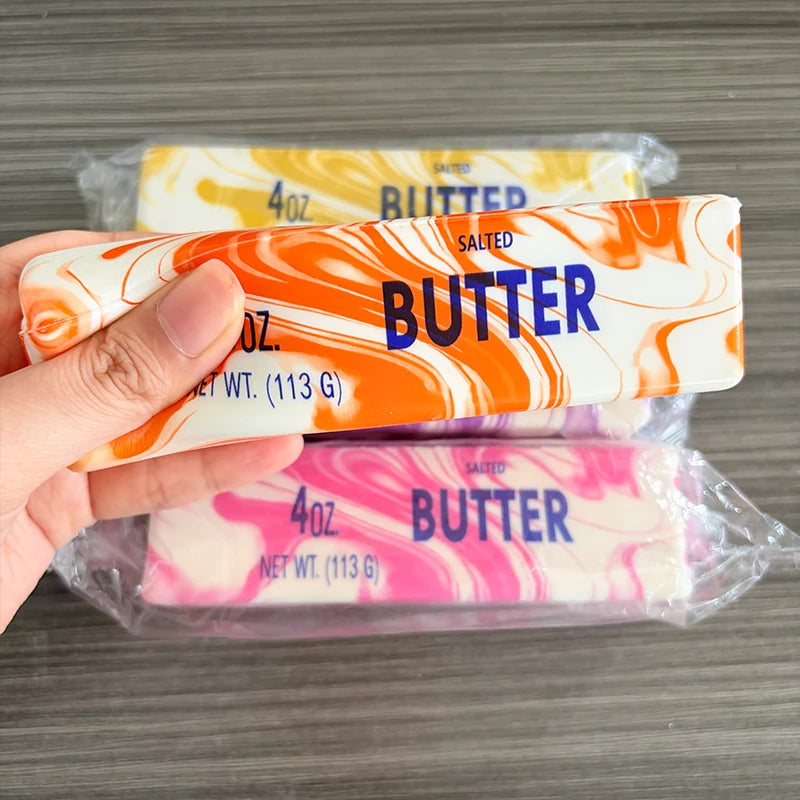 A hand holds a butter fidget stick squishy toy packaged in clear plastic.