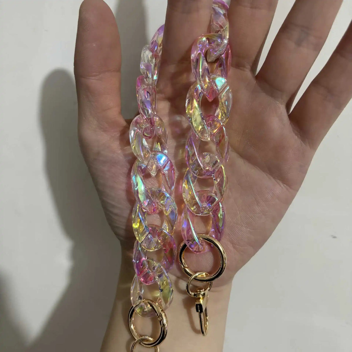A hand holds a long, colorful resin chain replacement strap with gold clasps.