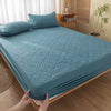 A teal quilted mattress protector with extra padding is displayed on a bed.