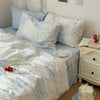 A light blue duvet cover set with white floral patterns and two matching pillowcases displayed on a bed.