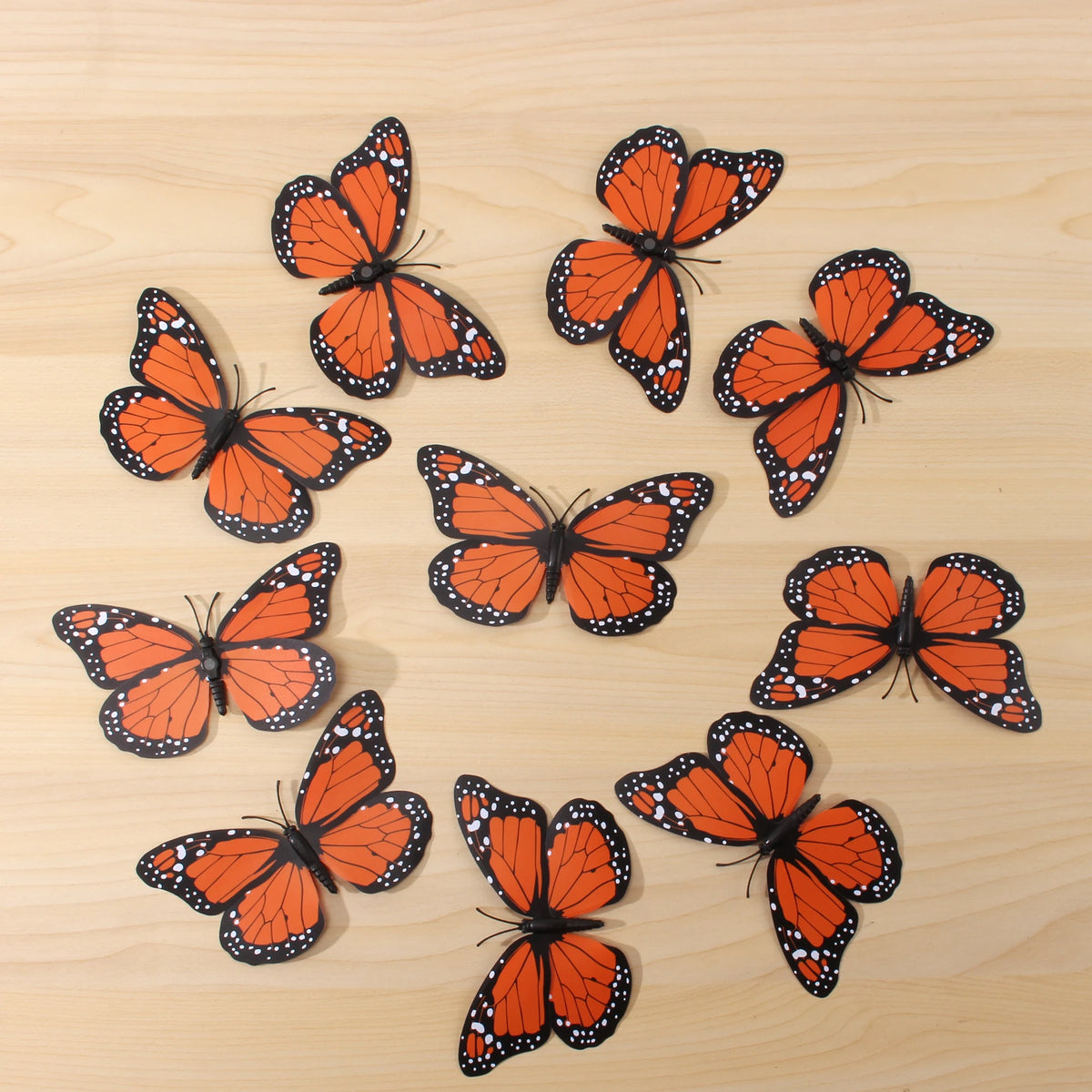 A collection of ten realistic orange and black monarch butterfly magnets scattered on a light wooden surface.