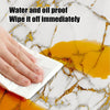 A hand wipes off oil and water from a yellow stain on white marble surface with a white cloth.
