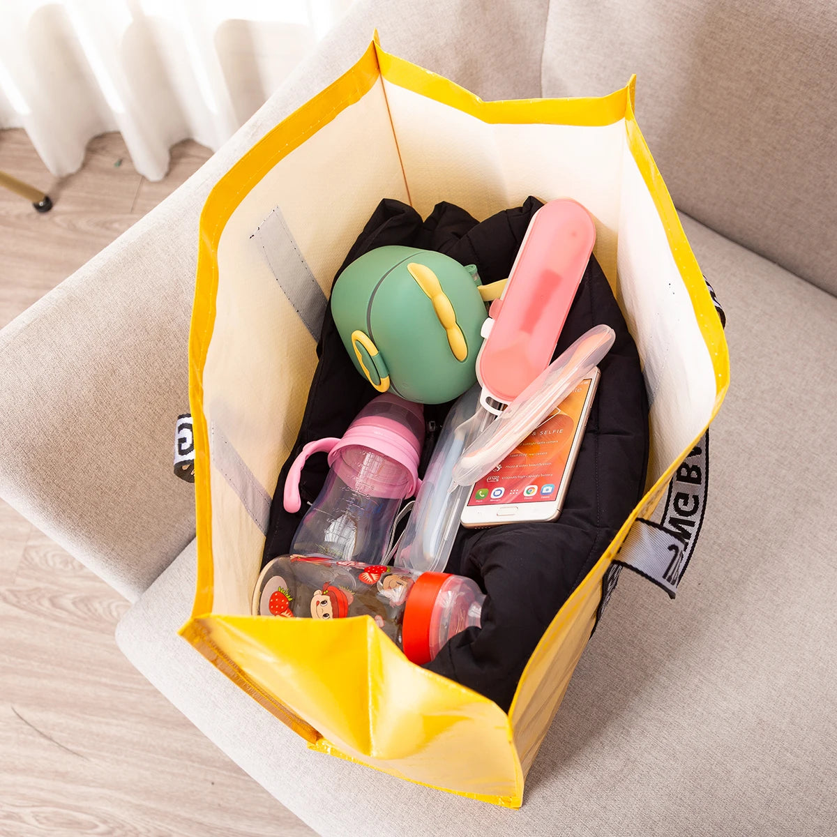 A yellow tote bag is open, containing various personal items like a green electronic device, pink bottle, and a smartphone.