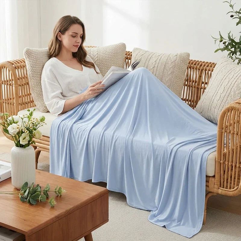 A woman is relaxing on a wicker sofa covered with a light blue ice silk blanket.