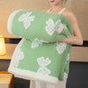 A person holds a light green plush jacquard throw blanket with white floral patterns.