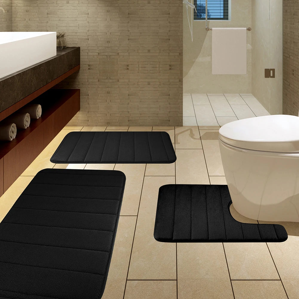 A set of black plush memory foam bath mats with non-slip backing placed on a tiled bathroom floor.