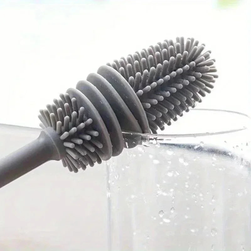 A silicone bottle brush with a long handle is shown cleaning the inside of a glass container.