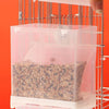 A hand is placing small seeds into a transparent anti-spill feeder housed within a metal grid.