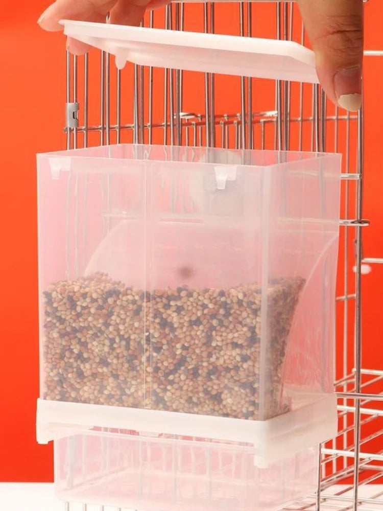 A hand is placing small seeds into a transparent anti-spill feeder housed within a metal grid.