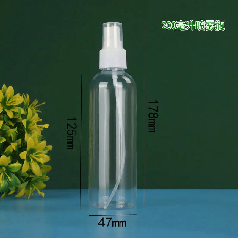 A clear glass spray bottle with a white pump dispenser and a yellow floral arrangement in the background.