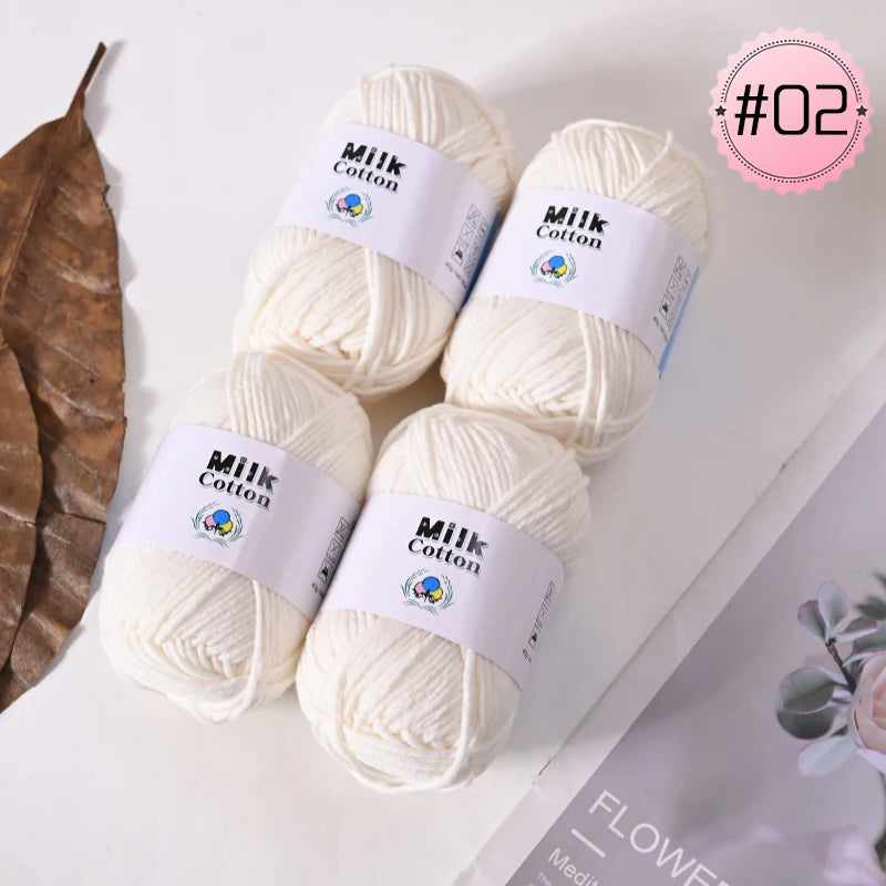 A pile of white Milk Cotton yarn balls is displayed on a white surface.